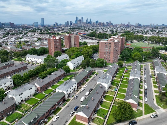 an aerial view of an affordable housing complex, featuring a mix of row houses and apartment buildings, with a city skyline in the background